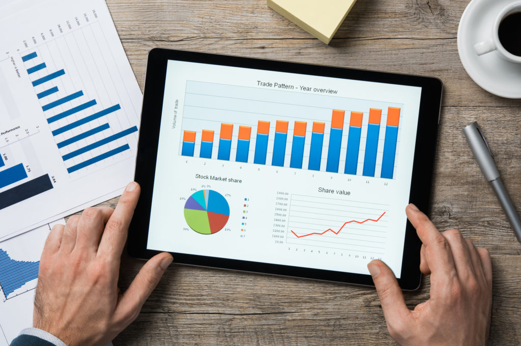 Top view of digital tablet with financial year overview on screen. Businessman analyzing investment charts with digital tablet on wooden desk at office. positive stock market trend.